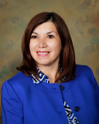 Headshot of Betty Balli Torres, wearing a bright blue jacket