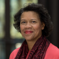 Portrait of Prof. Mechele Dickerson, wearing a pink shirt and pink and black scarf