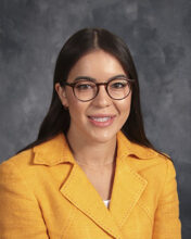 A headshot of a woman wearing a light orange jacket and a pair of glasses