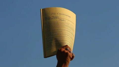 A hand holds a copy of the Constitution up in the air