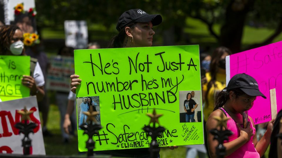 A woman holds a fluorescent green sign reading "He's not just a number, he's my husband"