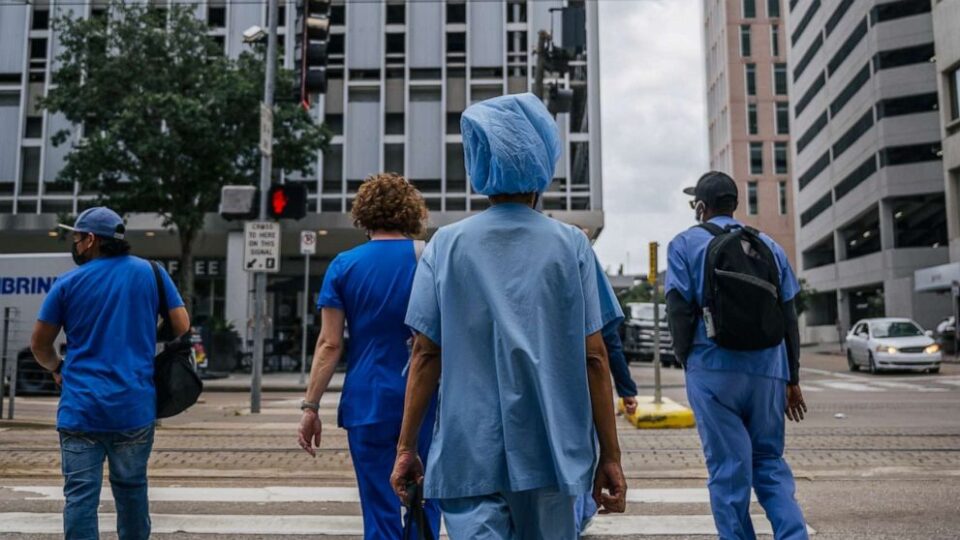 Hospital staff walking to Houston Methodist Hospital, wearing blue scrubs.
