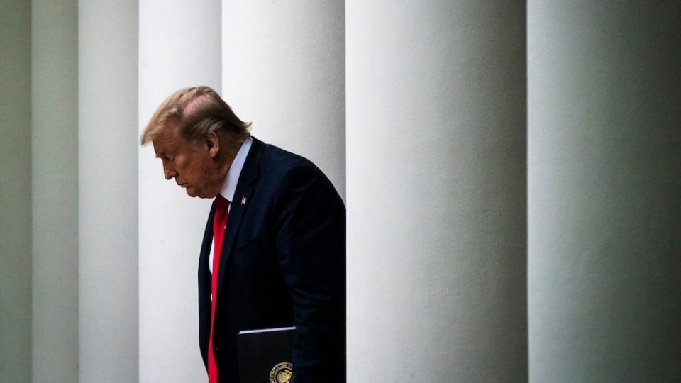 Donald Trump walks between columns, his head hung