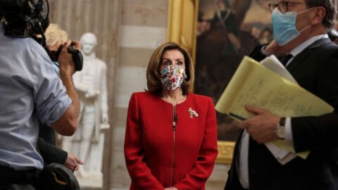 Nancy Pelosi looking forward, wearing a red jacket and floral mask.