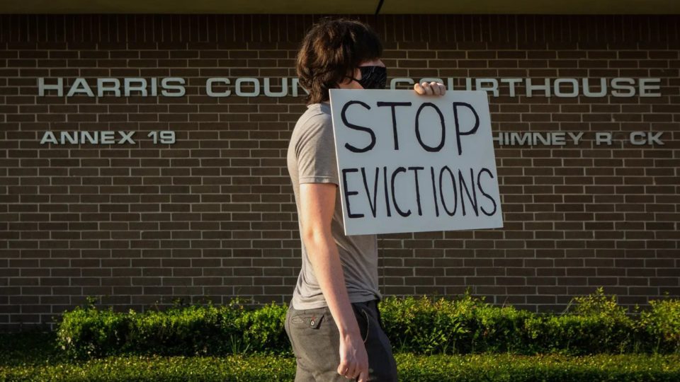 Man in front of the Harris County courthouse with a sign reading "Stop Evictions"