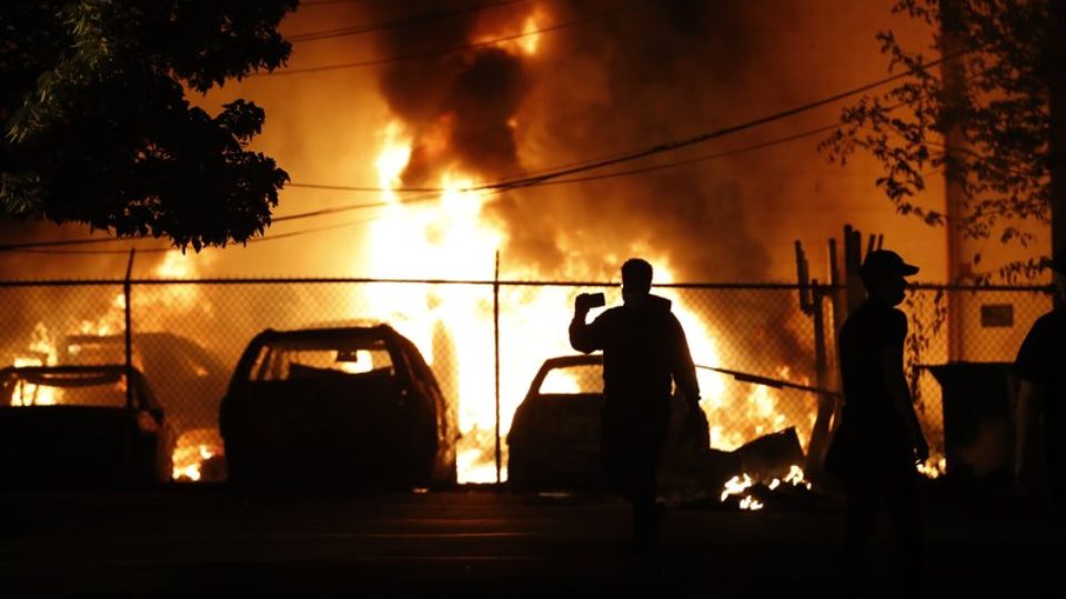 A silhouetted man uses a cell phone to film a raging fire near a parking lot