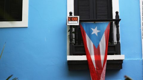 A Puerto Rican flag hangs from a window next to a SE VENDE sign