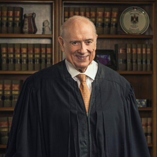 Formal photo of Judge Lamberth in black robe standing in front of case filled with books