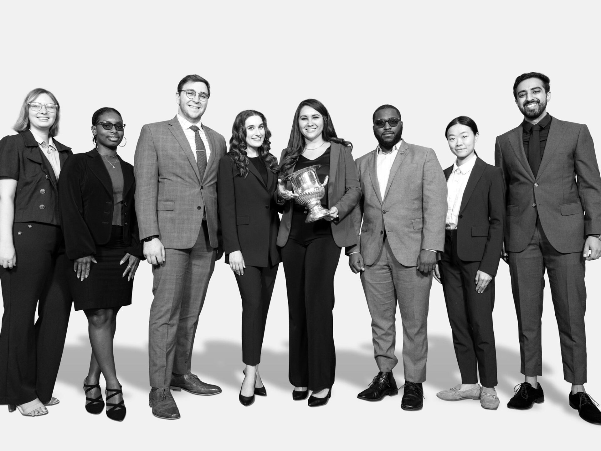 black and white photo of group of students in business suits holding a trophy