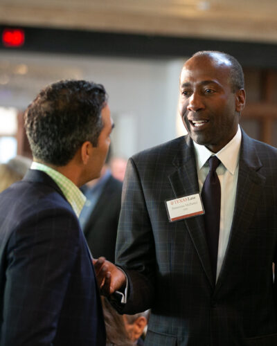 Man in a business suit speaks with others at a networking event. Demetrius G. McDaniel ’90 