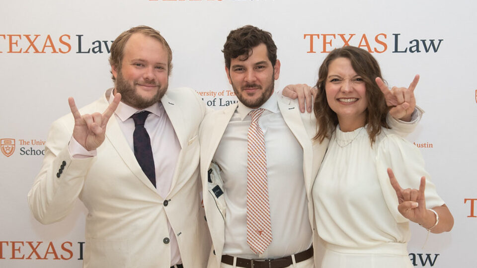 Three graduates wearing white suites in front of a Texas Law banner at the 2021 Sunflower Ceremony