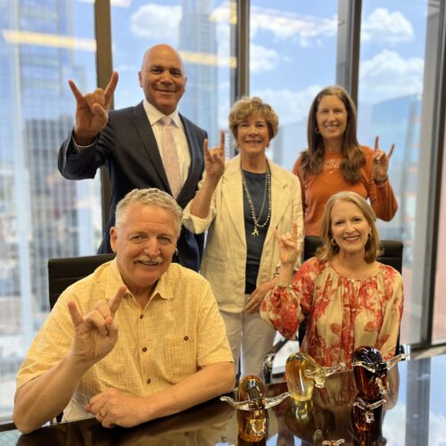 Five alumni pose with Hook Em signs