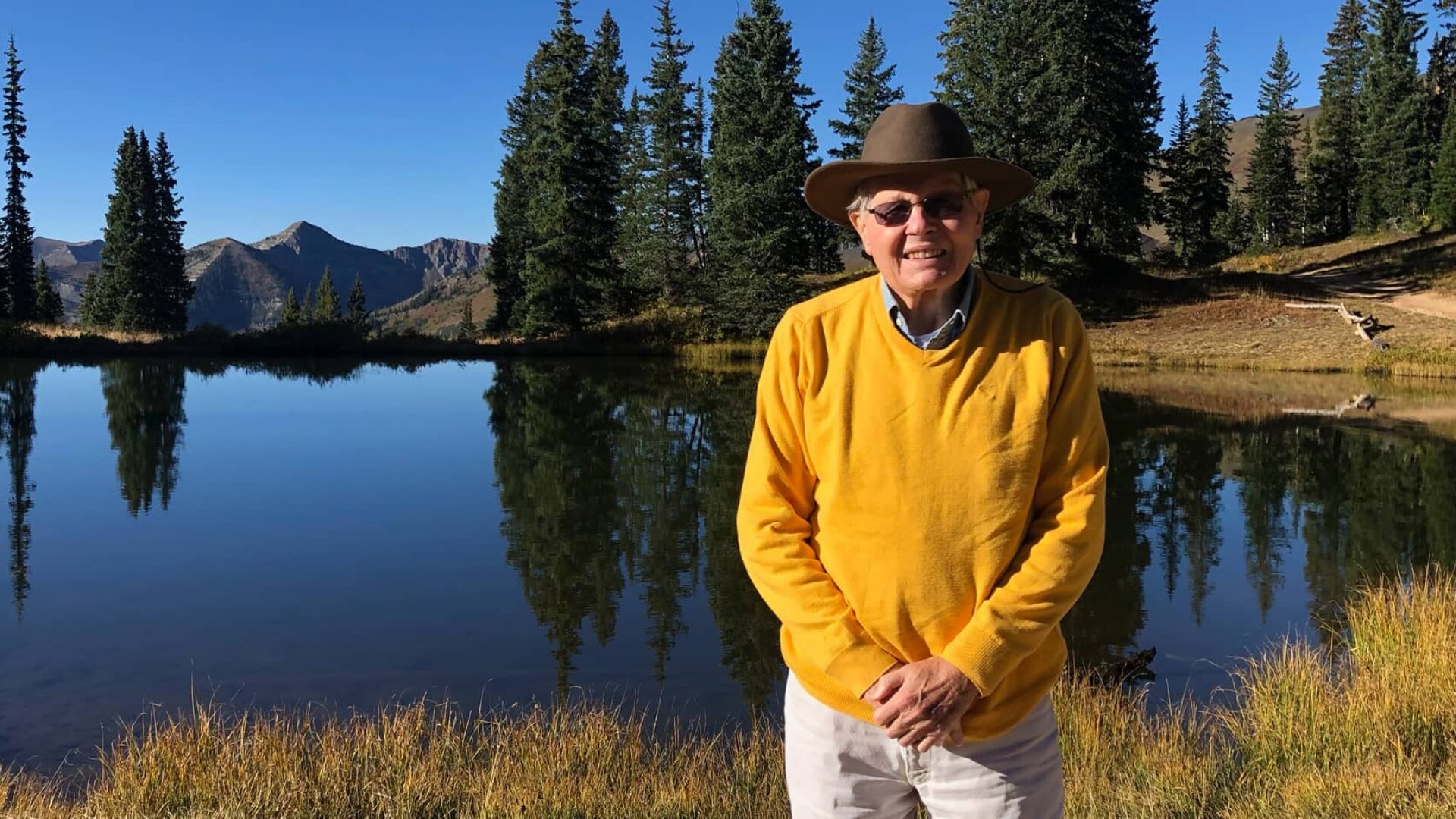 Photo of man wearing yellow sweater standing beside lake
