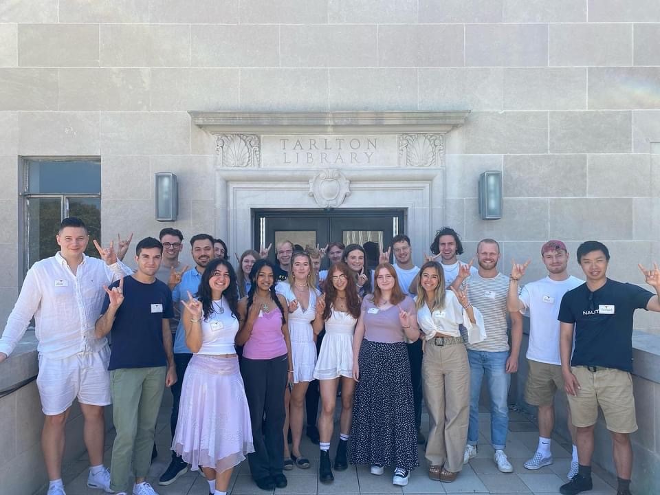 A group of 21 LLM students pose outside the law school using the "hook 'em Horns" hand gesture.